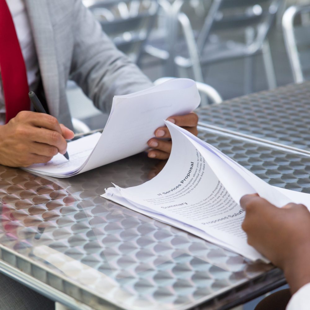 Business partners checking and signing documents in street cafe. Closeup of papers and writing business man hand. Deal or paperwork concept